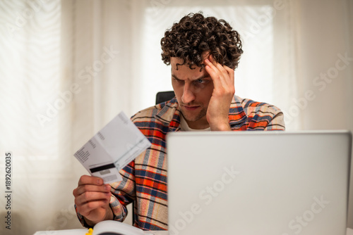 Wallpaper Mural Stressed and depressed young man using laptop and credit card to pay bills while sitting at his home. He is having financial problems.	 Torontodigital.ca