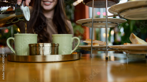 Fotografía Woman pouring tea into a mug at a table with pastries and a tiered stand