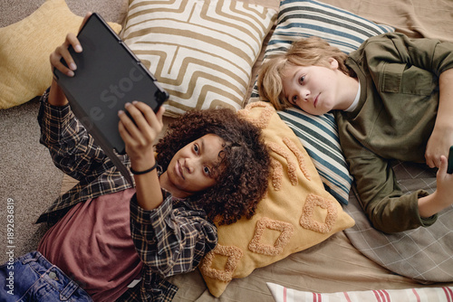 Quadro su tela Two Generation Alpha kids lying on pillows using digital tablet together, Black