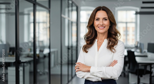 Confident businesswoman standing in modern office with arms crossed and smiling at camera, surrounded by glass partitions and workstations Free Download Confident businesswoman standing in modern office with arms crossed and smiling at camera, surrounded by glass partitions and workstations - GFXLoad