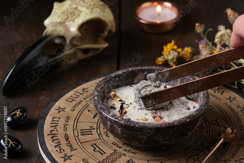 Foto Wicca incense ritual - placing a glowing charcoal with tongs in an incense burne