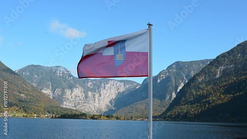 Austrian national flag waving with Hallstatt Lake and alpine mountains in the background. Scenic travel destination in Austria.