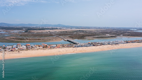 Aerial view captures Praia de Faro with its sandy beach, shoreline, and bridge over Ria Formosa on a sunny day in Portugal