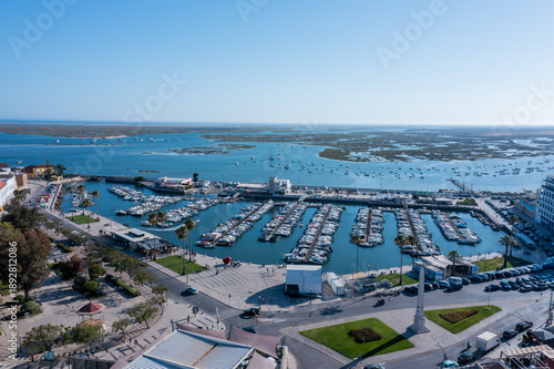 Visitors explore the Ria Formosa in Faro, Algarve, with boats docked and the waterfront bustling under a sunny sky in the background
