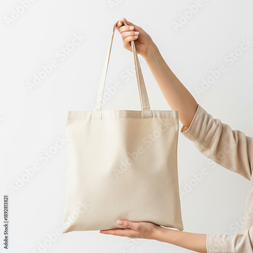 Woman's hand holding a plain canvas tote bag, white background, clean mockup