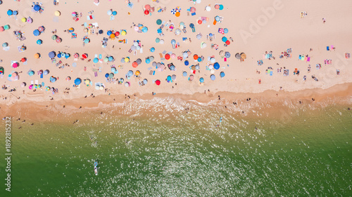 Obraz na plátne Aerial view of vibrant beach scene with colorful umbrellas, sunbathers, and clear water, capturing summer leisure and relaxation