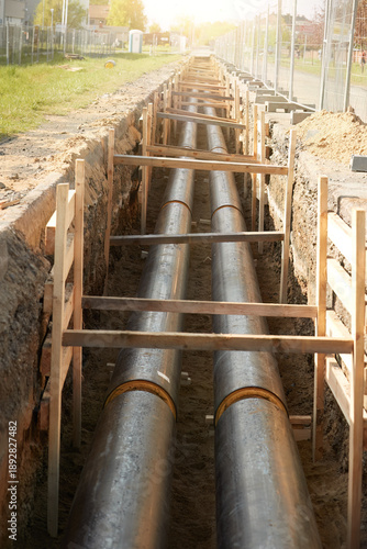 Industrial site showcasing the installation of pre-insulated steel pipelines in a trench. Ideal for: district heating project reports, energy efficiency articles, and utility maintenance news.