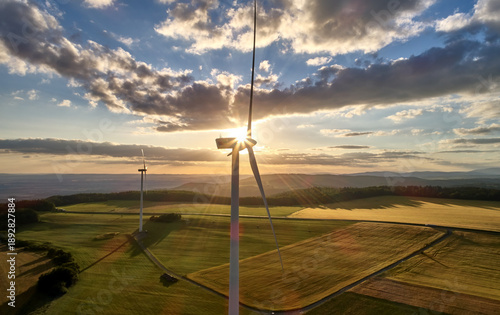 Wind turbines producing renewable electricity at sunset above agricultural landscape. Ideal for: clean energy, sustainability, energy transition, smart grid, decarbonization concepts. 