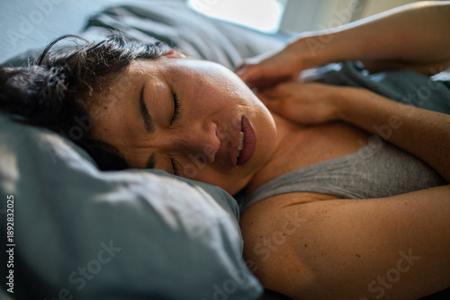 Woman with neck pain waking in bed at home