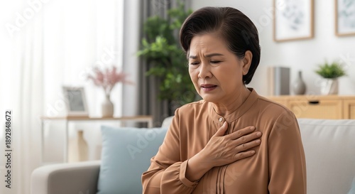 An elderly Asian woman is experiencing chest pain, clutching her chest with a pained expression, suggesting a potential medical emergency. Free Download An elderly Asian woman is experiencing chest pain, clutching her chest with a pained expression, suggesting a potential medical emergency. - GFXLoad