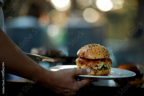 Waiter serving gourmet burgers at an outdoor venue. Ideal for: catering service websites, hospitality marketing brochures, and food event social media posts.