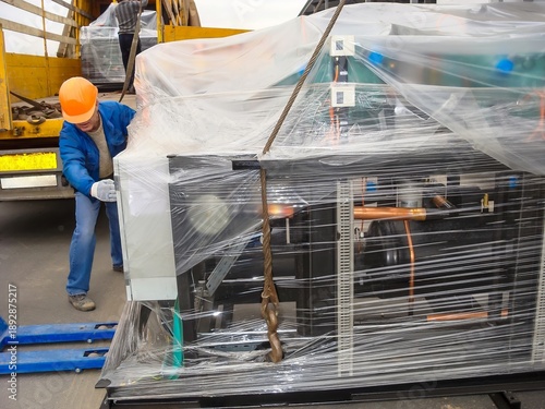 A worker is carefully unloading a large industrial chiller from a truck using a pallet jack.