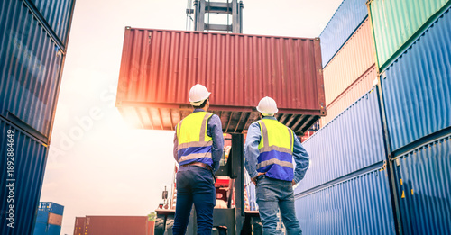 Two Engineer or foreman wears PPE checking container storage with cargo container background at sunset. Logistics global import or export shipping industrial concept.
