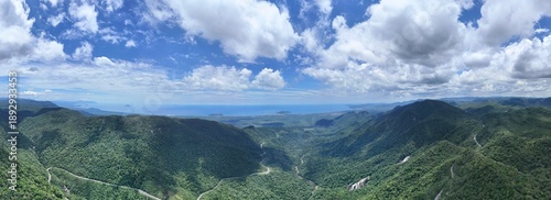 Foto Paisagem panorâmica de montanhas verdes e vale profundo sob céu azul com nuvens, mostrando natureza preservada, relevo serrano e cenário natural ideal para turismo e aventura