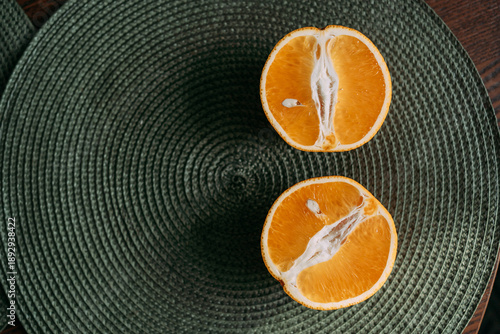 Two orange halves on a round woven placemat, top view, warm natural light