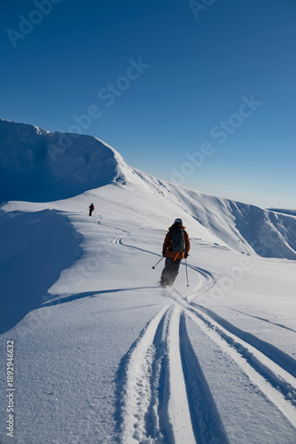 Fotografie Two skiers trek through fresh powder on an alpine ridge under a clear blue sky