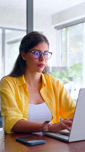 Smiling latin hispanic female marketing manager, professional it specialist working, browsing at laptop computer sitting at desk in modern office. Young woman employee using pc for business. Vertical