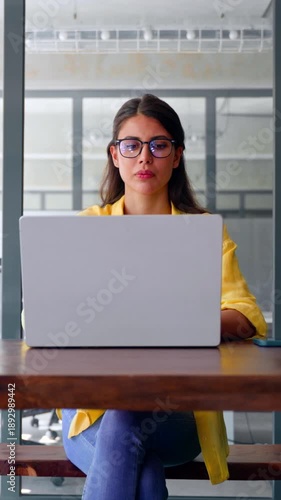 Thinking latin hispanic female marketing manager, professional specialist looking at screen working at laptop computer sitting in office. Young woman student using pc for business studying. Vertical