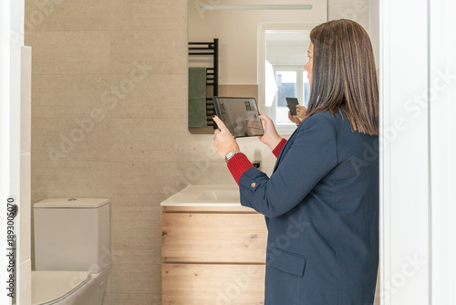 Realtor holding a tablet, recording a virtual tour of a modern bathroom