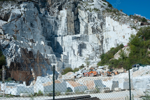 Active marble quarry with white rock face, heavy machinery and stone blocks, mining and construction industry