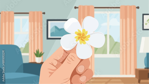 A hand holds a white flower with a yellow center in a cozy room