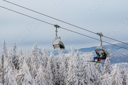 Chairlift with skiers over snowy forest in Poiana Brasov, Romania