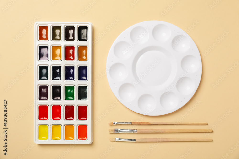 Obraz premium Watercolor paints, palette and brushes on beige background, flat lay
