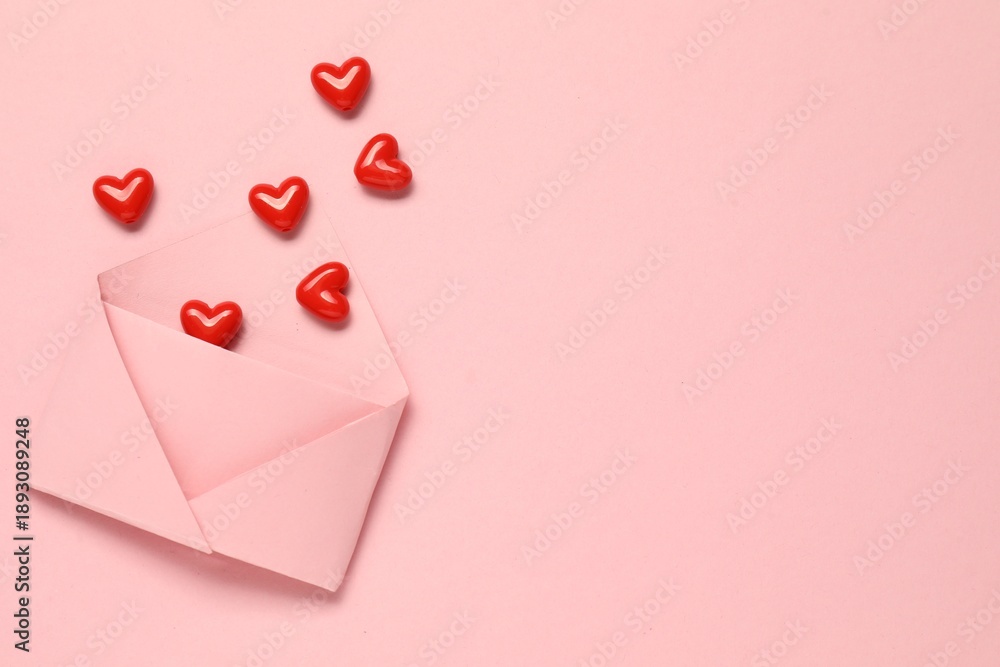 Naklejka premium Love. Envelope with red decorative hearts on pink background, flat lay. Space for text