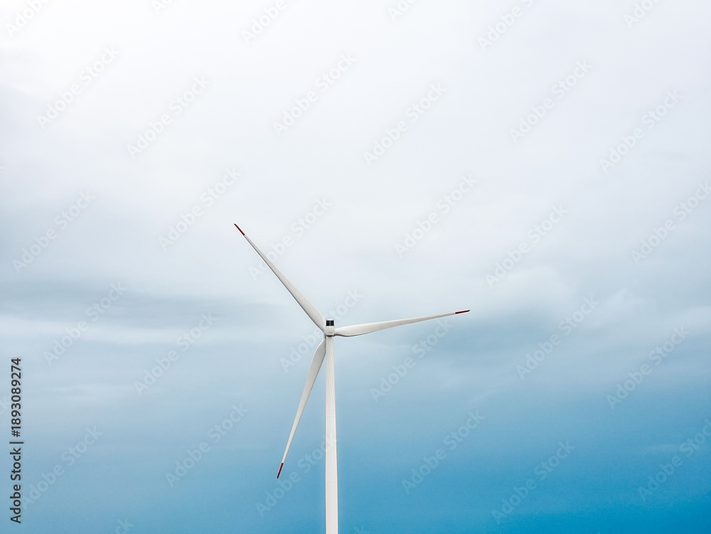 Fototapeta premium Single wind turbine against soft cloudy sky. Minimal renewable energy concept with copy space. Clean electricity production, sustainable technology and environmental power generation.