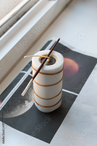 Minimalist still life of unlit wax candle with wick on windowsill, cozy home decor and soft natural light