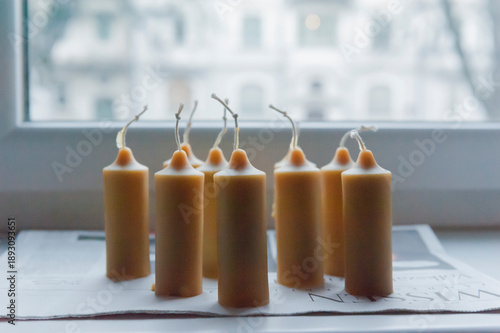 Handmade beeswax candles cooling by the window, natural wax pillars with wicks, cozy DIY candle making workshop