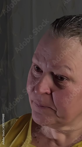Middle-aged caucasian lady coloring her hair. White rubber gloves. White and gray background. Using hair dye. Camera slowly moving around. Vertical video.