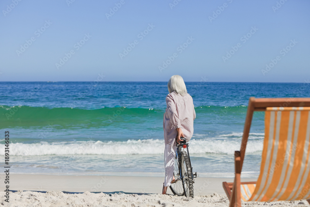 Fototapeta premium Bicycle is leaning in wet sand near striped orange-and-white chair while waves are lapping