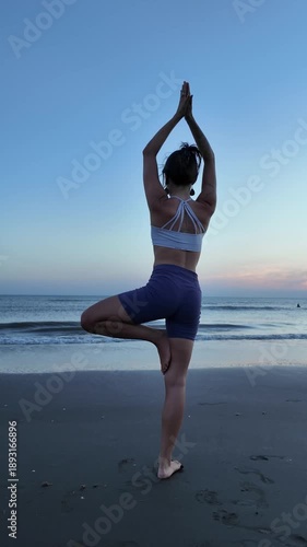 Lesbian woman practicing yoga tree pose on the beach at sunset
