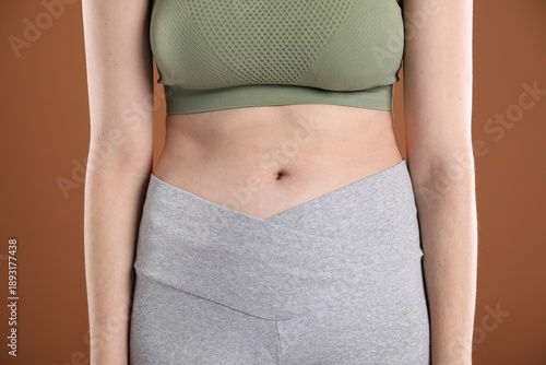 Woman in sportswear after weight loss on brown background, closeup