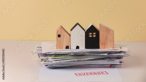 Fotografie Overdue mortgage concept with stack of bills and wooden house models illustratin
