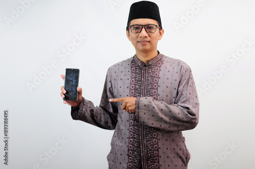 An Asian Muslim man smiles happily while sending a message using his mobile phone, isolated on white background