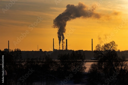 Fotografie Silhouetted industrial smokestacks belch thick plumes against a vibrant golden s