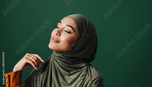 Serene stylish woman wearing green hijab smiling softly with eyes closed expressing calm elegance in studio portrait