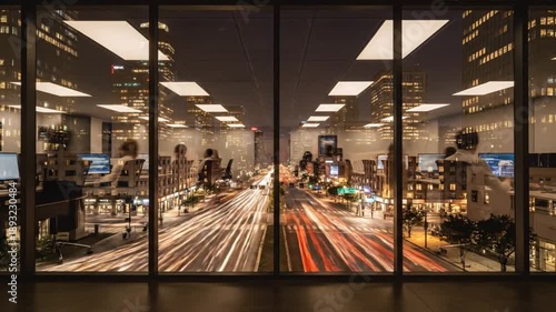 Nighttime view through office windows of a busy city street with blurred traffic lights and cars, reflecting urban activity and office lighting.