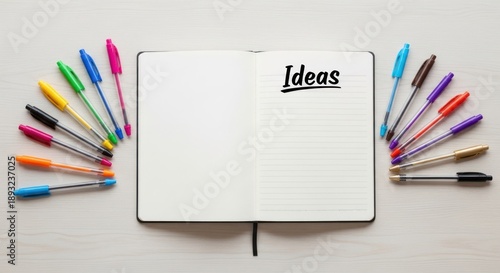 A white notebook with the word 'Ideas' written on it, surrounded by a variety of colored pens on a wooden surface.