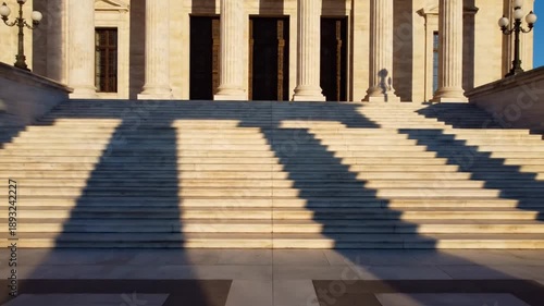 Wide-angle shot of a large stone staircase with columns and a person walking in the background, casting long shadows in a formal, architectural