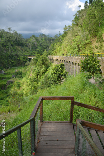 Plunyon Kalikuning is a popular riverside park featuring a historic bridge, hiking trails, and panoramic views of the green hills and mountains