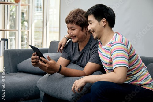 Wallpaper Mural Happy LGBTQ Asian couple enjoying digital content together on tablet while sitting on sofa at home, showing love, relaxation, and technology connection in daily lifestyle Torontodigital.ca