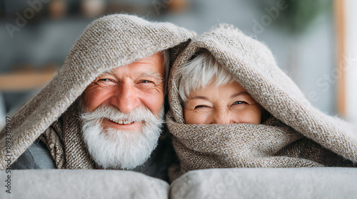 A smiling older couple cuddled on a couch under a blanket, capturing cozy living, winter comfort, and a relaxed retirement lifestyle.