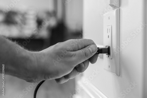 Foto Hand plugging power cable into American wall outlet in modern home interior, clo