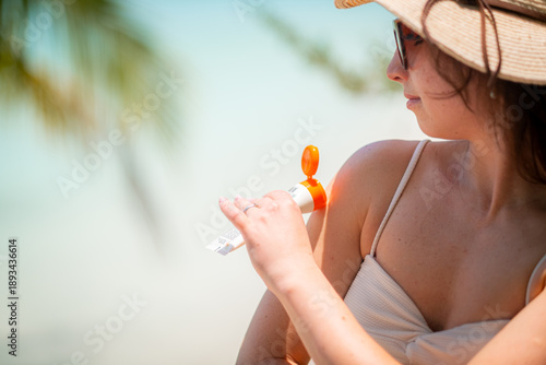 woman applies sunscreen on bright beach, wearing straw hat and relaxed posture, enjoying sunny day., wellness, summer, health, protection., Summer vacation, sun care., World Health Day