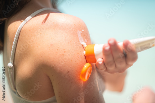 woman applies orange sunscreen to her arm outdoors, focusing on pump dispenser, in blurred blue background, care, health, skincare, summer., wellness, protection, sun, beach., summertime