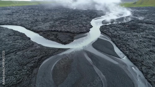 Aerial view of a river cutting through dark, textured volcanic landscape