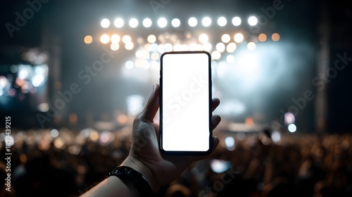 Hand holding smartphone with blank screen at a live music concert with a crowd in the background